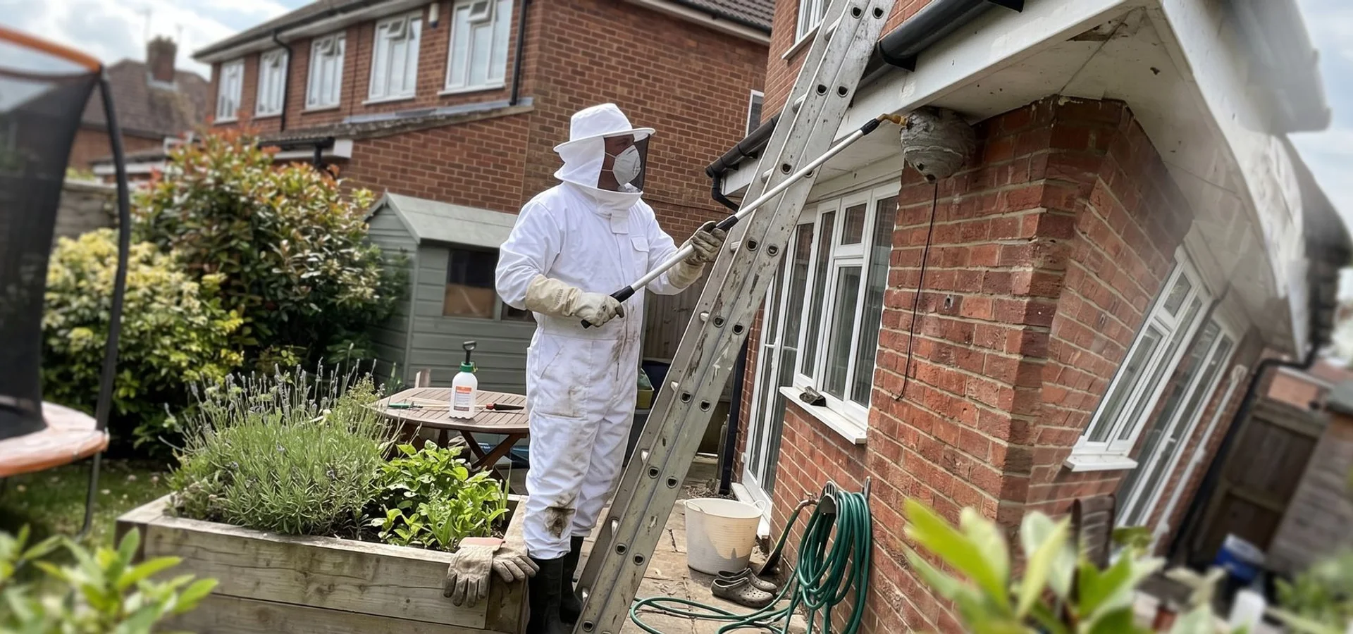 Pest control technician in a protective suit treating a wasp nest in the eaves of a Surbiton home